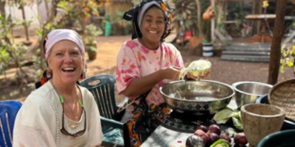 Two women sit outside at a table preparing food.