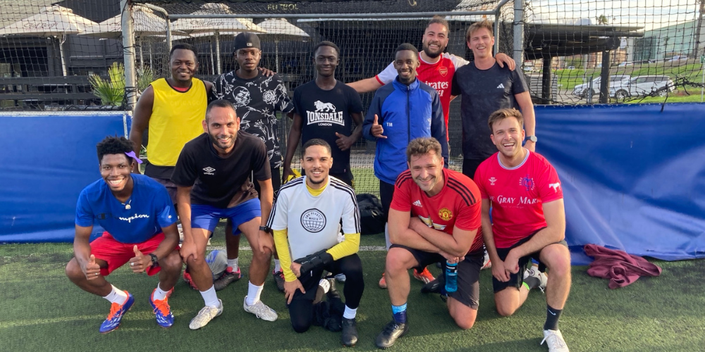 A group of guys in soccer uniforms pose for a group shot on a soccer field