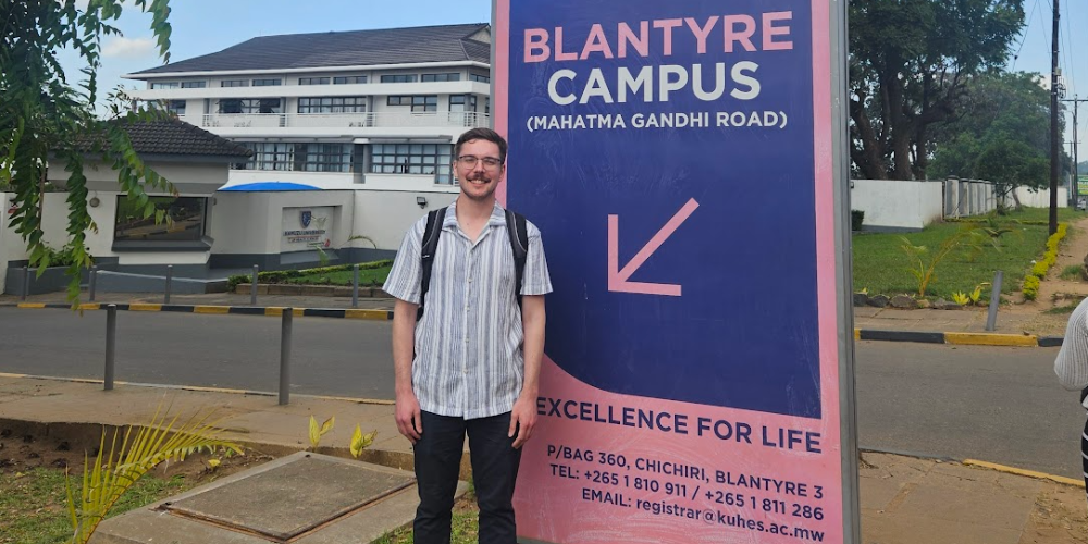 A student stands beside a campus sign in Blantyre