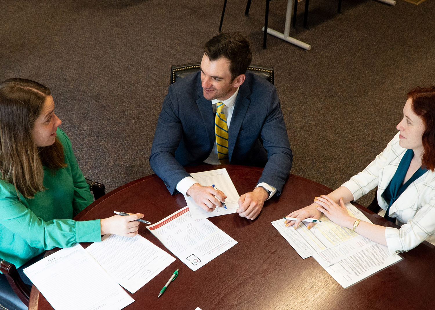 three professionals at a round table talking, papers spread around