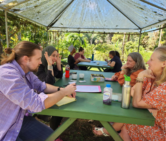 Faculty sit outside at a picnic table talking