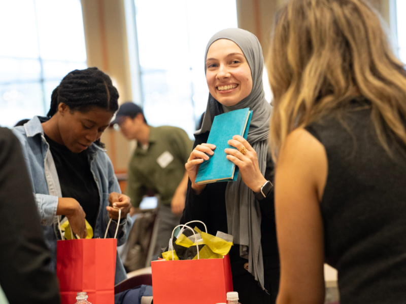 A student wearing a hijab holds a journal while other students examine gift bags