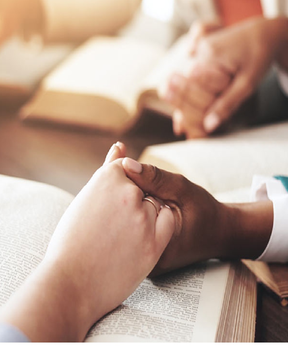 Two people holding hands while in prayer.