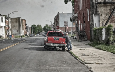 under-resourced urban neighborhood, two men talk beside an red pick-up truck