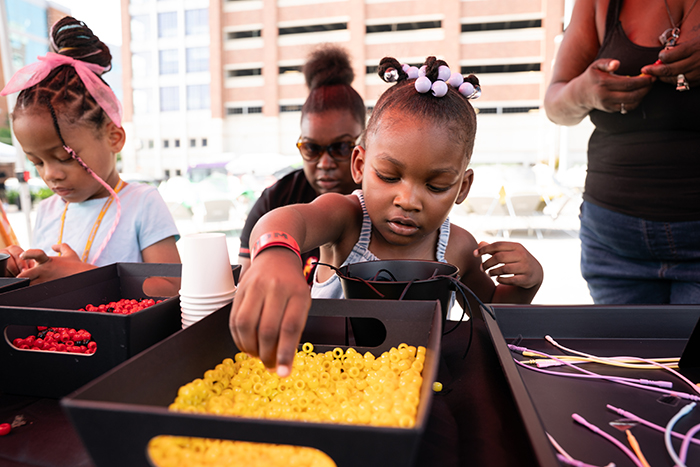 A young attendee carefully strings beads to make a custom keychain at OCCE’s Juneteenth Jubilee.